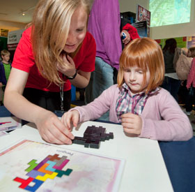 A University of Edinburgh student helps a girl with the pentominoes exhibit during a science festival